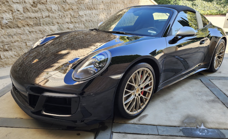 Glossy black Porsche 911 Targa with detailed paint parked outside a stone wall